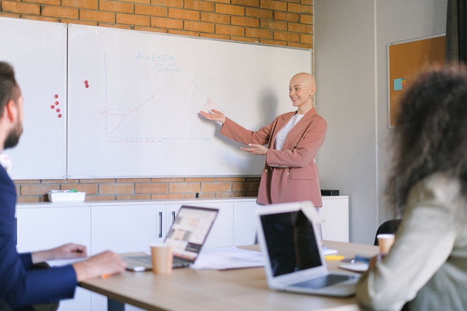Smiling bald female demonstrating schemes of business plan to colleagues at table with laptops in boardroom