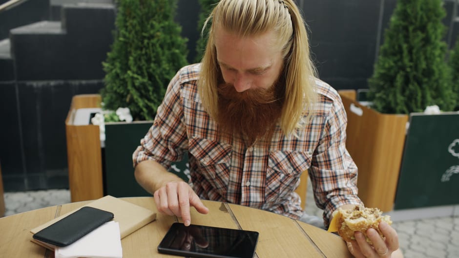 Bearded man using a tablet while having a coffee break at an outdoor cafe.
