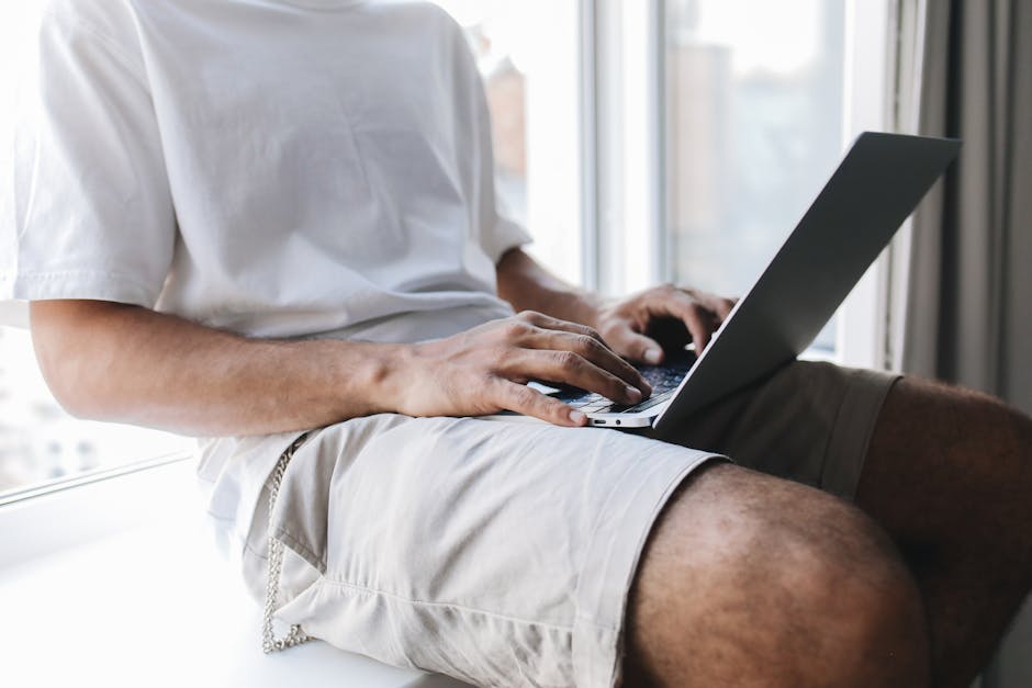 Person sitting by window using laptop, showcasing a casual and relaxed home workspace.