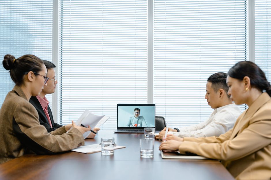 Four colleagues in a conference room engaged in a meeting with remote participant on video call.
