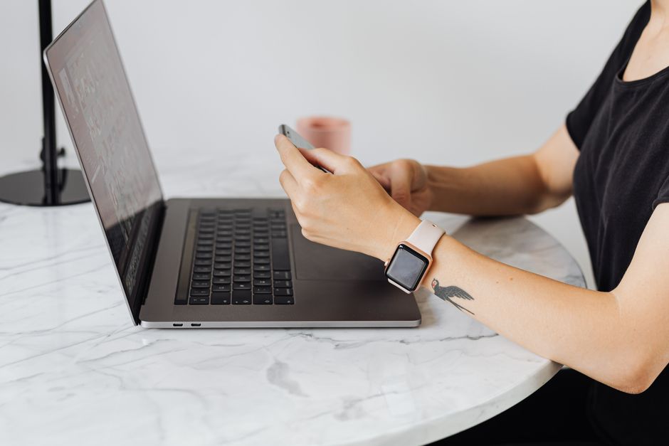 Adult using smartphone and laptop simultaneously at a marble table indoors.