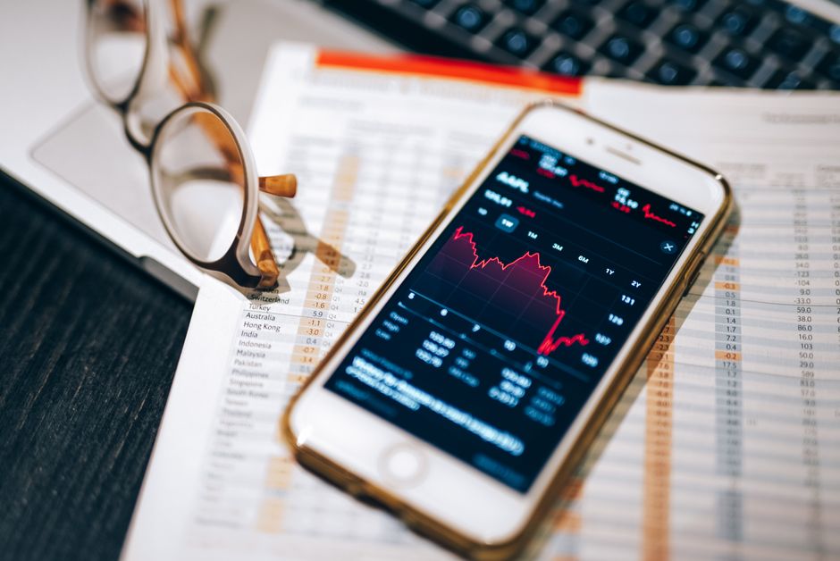 Smartphone displaying stock market chart on a financial spreadsheet with eyeglasses.
