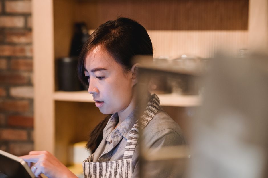 Woman in apron using tablet in a café setting, deeply focused on work.