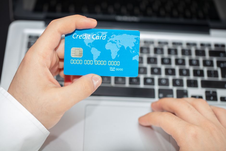 Person holding credit card near laptop for online shopping, emphasizing secure online transactions.