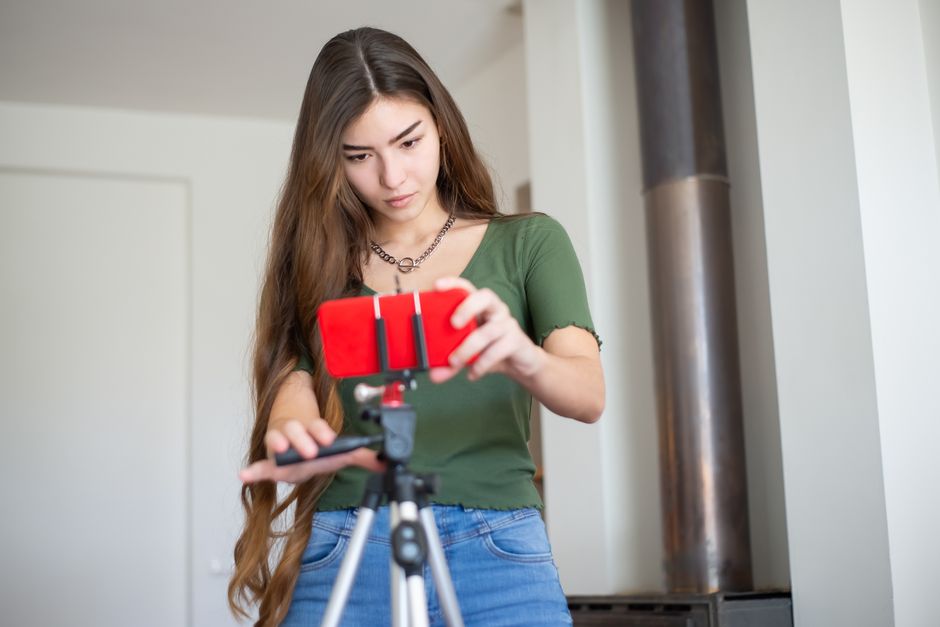 Young woman adjusting smartphone on tripod indoors, focusing on content creation.