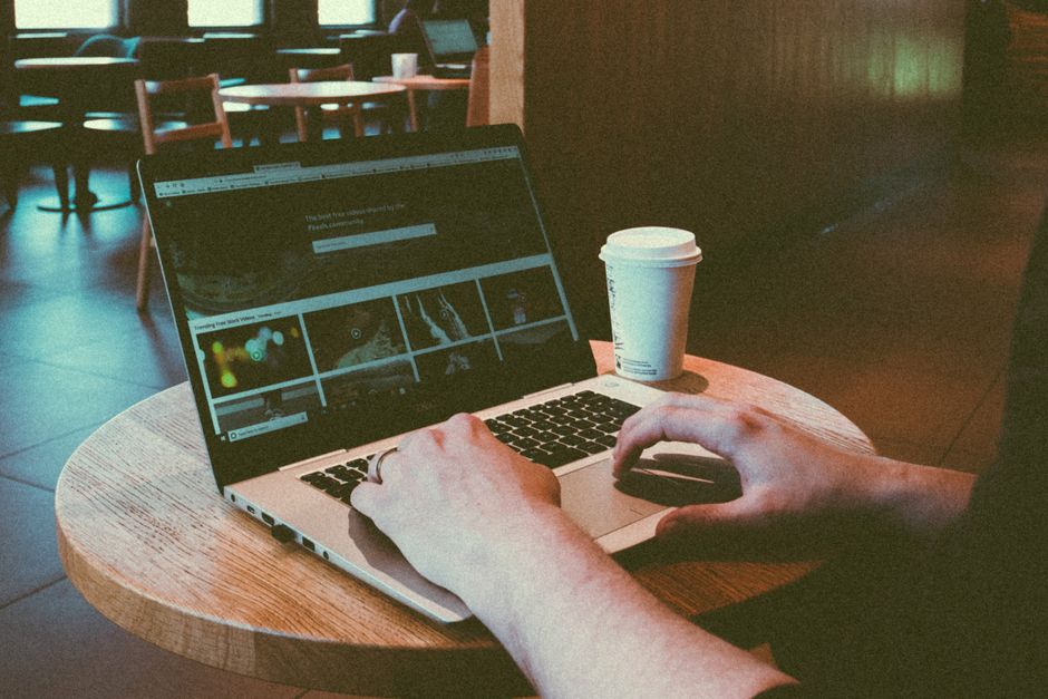 Person using a laptop in a cozy café, highlighting remote work lifestyle with a coffee cup on the table.