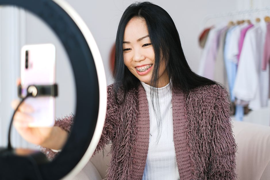 Smiling woman using smartphone and ring light for live streaming indoors.