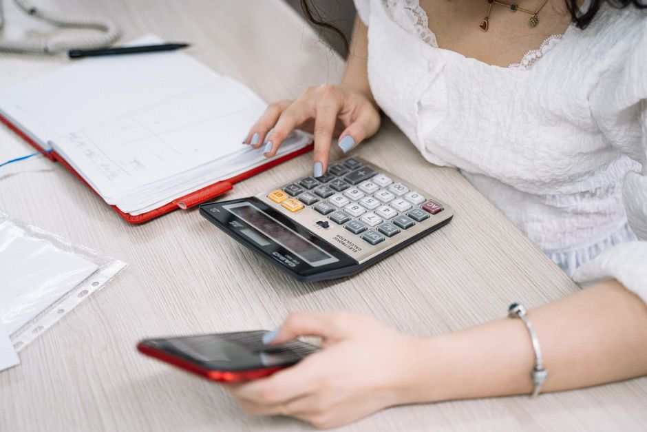 Close-up of a woman using a calculator and phone at her office desk.