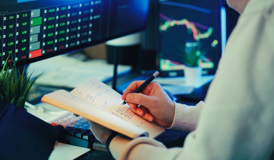 Person analyzing financial data on screens, making notes. Ideal for business and finance themes.