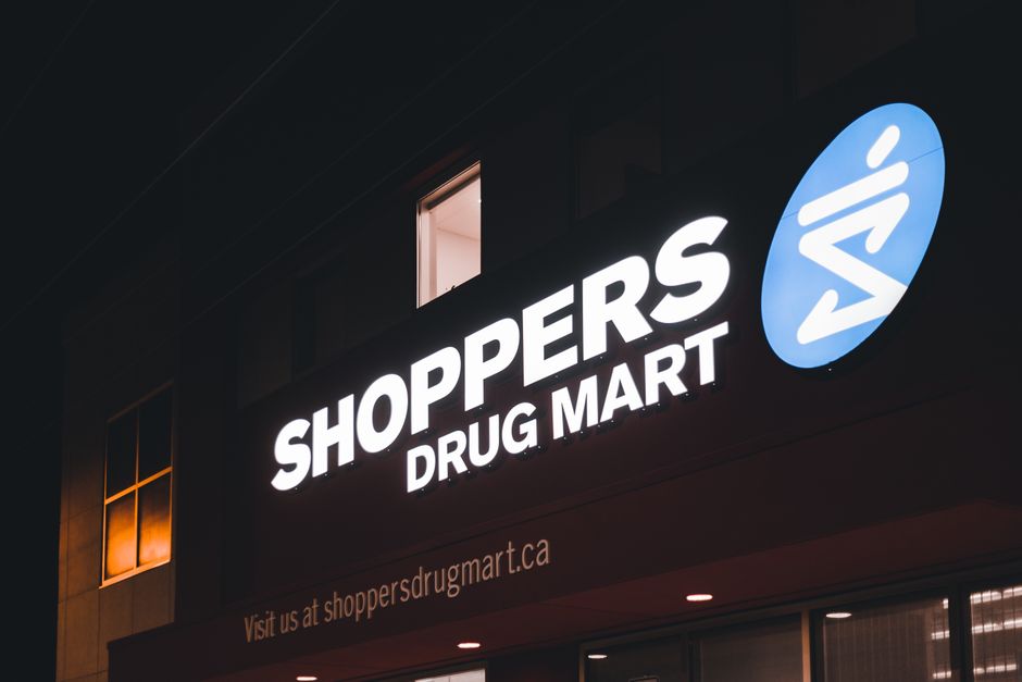 Brightly lit Shoppers Drug Mart sign on building exterior at night, urban setting.