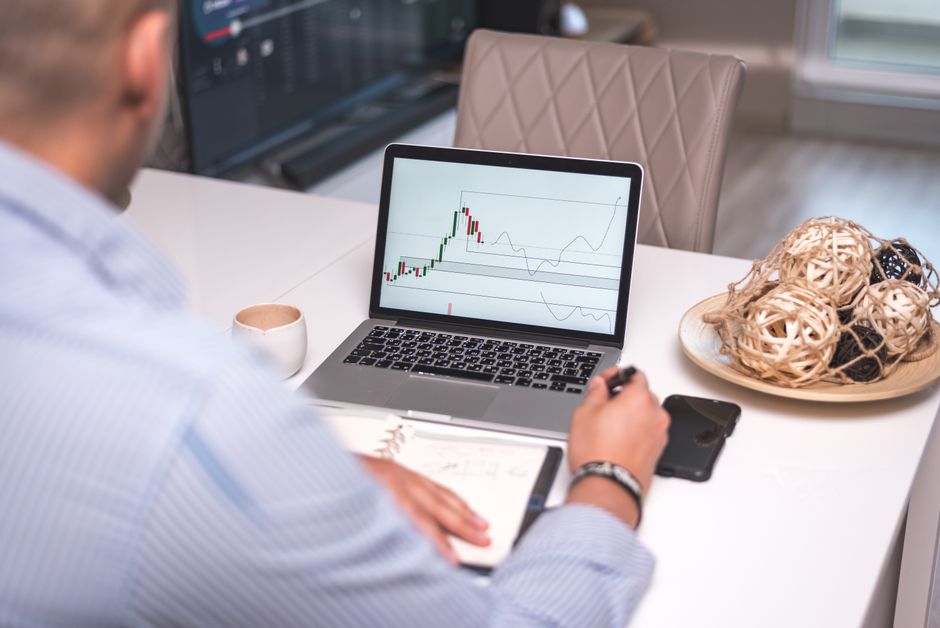 Man studies financial graphs on a laptop at a modern home office setting, focusing on market analysis.