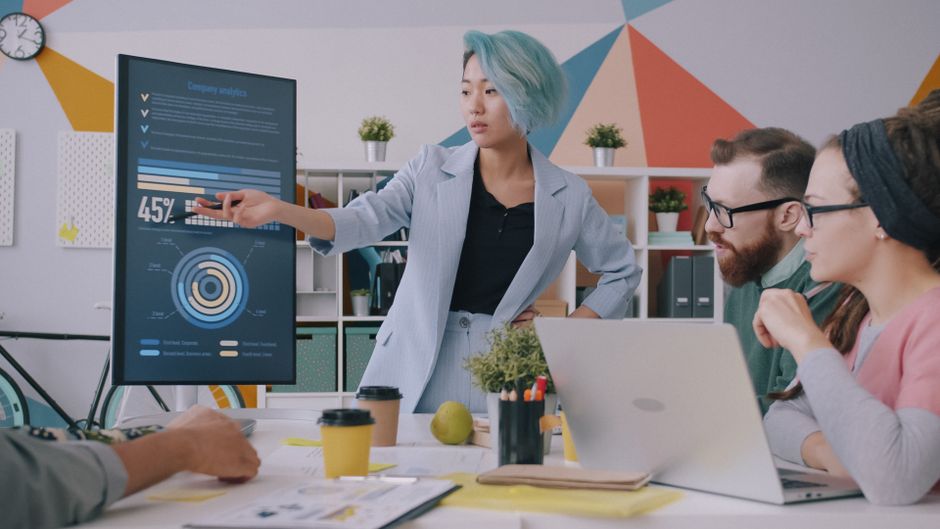 Diverse team meeting with data presentation on screen in modern office setting.
